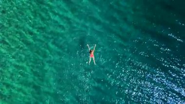 Pembe mayo giymiş bir kadının hava görüntüsü kristal berrak deniz sularında yüzüyor, rahatlatıcı bir şekilde. Yaz tatilleri.