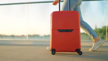 Kadın yalnız seyahat ediyor. Bir gezgin gün batımında şık kahverengi bavullarıyla havaalanı terminalinde geziniyor. Yaz tatili kavramı. Ağır çekim. Yan görünüm