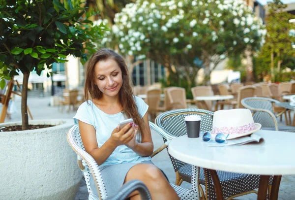 Woman relaxing in the outdoor cafe - drinking coffee and using a — Stock Photo, Image