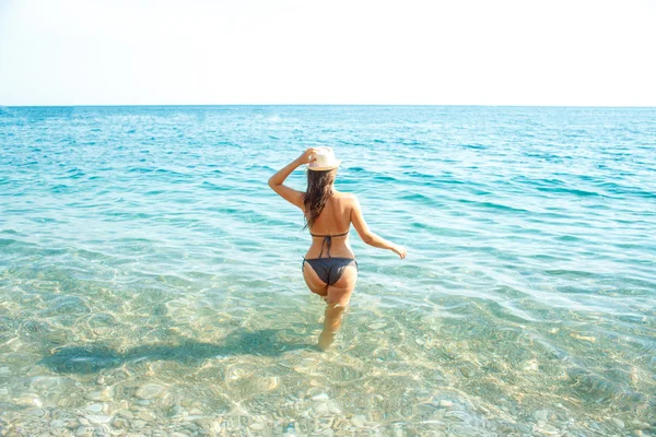 Mujer con sombrero de sol y bikini de pie con el brazo levantado hacia ella —  Fotos de Stock