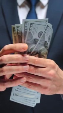 Resmi olarak giyinmiş bir adam Amerikan dolarlarını sayıyor, yakın plan. Yatırım, başarı, finansal beklentiler veya kariyer ilerlemesi kavramı.
