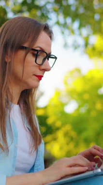 Kadın parkta oturuyor ve bir dizüstü bilgisayar üzerinde çalışıyor..