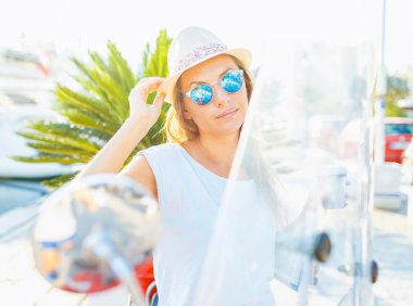 Happy young woman drinking takeaway coffee near her red moped in