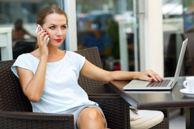 Bir dizüstü bilgisayar ile bir kafede oturan ve konuşurken çekici kadın