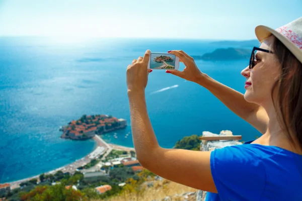 Girl  making photos by the smartphone island of Sveti Stefan, Mo — Stock fotografie