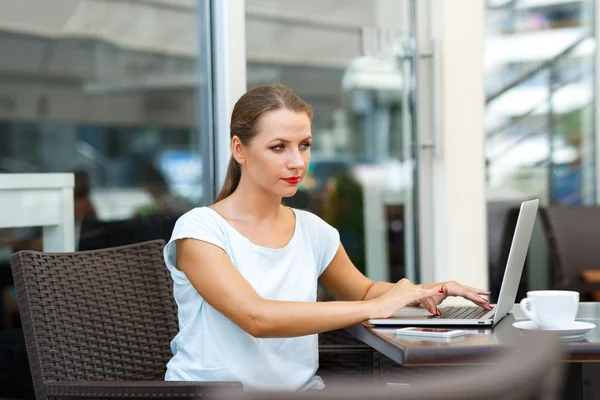 Joven mujer de negocios sentada en un café con una computadora portátil y café — Foto de Stock