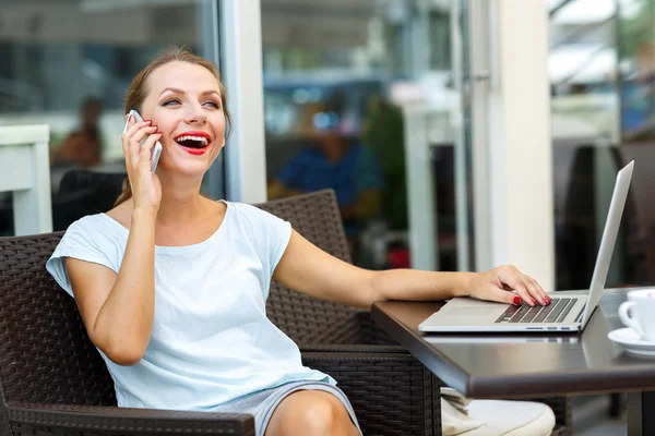 Attractive woman sitting in a cafe with a laptop and talking on — Stock Photo, Image