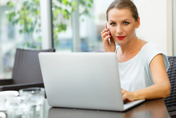 Mujer atractiva sentada en un café con una computadora portátil y hablando en — Foto de Stock