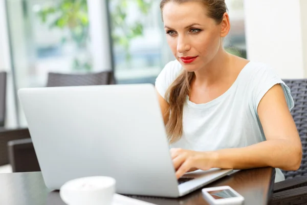 Joven mujer de negocios sentada en un café con una computadora portátil y café — Foto de Stock