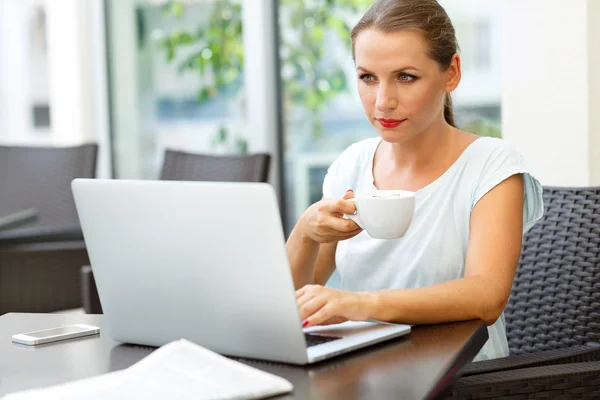 Giovane donna d'affari seduta in un caffè con un computer portatile e bevande — Foto Stock