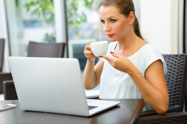 年轻的商界女人坐在一台笔记本电脑和饮料的咖啡馆 — 图库照片
