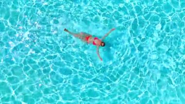 Pembe mayo giymiş bir kadının havuzda sırt üstü yüzüşü. Rahatlatıcı konsept, yaz yaşam tarzı. Yavaş çekim