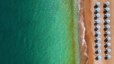 Mavi güneş şemsiyeleri ve turkuaz deniz suyuyla cennet gibi kumlu sahil manzarası..