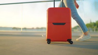 Kadın yalnız seyahat ediyor. Bir gezgin gün batımında şık kahverengi bavullarıyla havaalanı terminalinde geziniyor. Yaz tatili kavramı. Ağır çekim. Yan görünüm