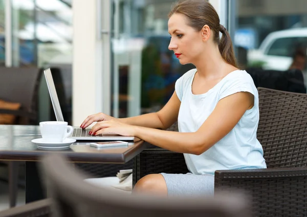 Atractiva mujer de negocios sentada en un café con un ordenador portátil y co — Foto de Stock