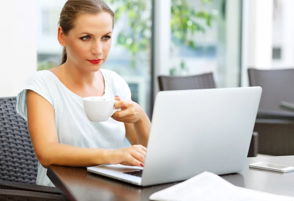 Atractiva mujer de negocios sentada en un café con una computadora portátil y dr — Foto de Stock