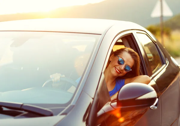 Leende kvinna kör bil vid solnedgången — Stockfoto