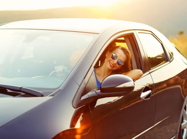 Femme souriante conduisant une voiture au coucher du soleil — Photo