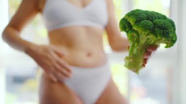 Bir kadın elinde bir brokoli tutuyor. Karnını okşuyor ve baş parmağını kaldırıyor. Sağlıklı beslenme ve sindirim kavramı