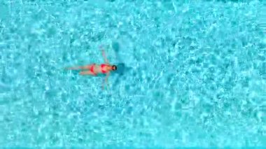 Pembe mayo giymiş bir kadının havuzda sırt üstü yüzüşü. Rahatlatıcı konsept, yaz yaşam tarzı.