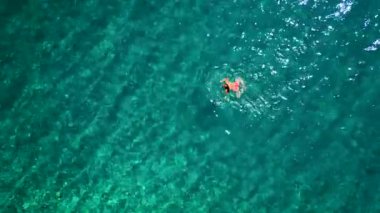 Pembe mayo giymiş bir kadının hava görüntüsü kristal berrak deniz sularında yüzüyor, rahatlatıcı bir şekilde. Yaz tatilleri.