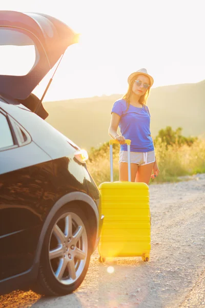 Žena s žlutým kufrem stojící poblíž kufru auta pa — Stock fotografie