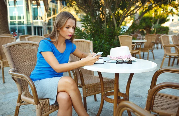 Immagine candida di una giovane donna che utilizza smartphone e prende appunti i — Foto Stock