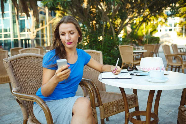 Candid image of a young woman using smartphone and makes notes i — Stock Photo, Image
