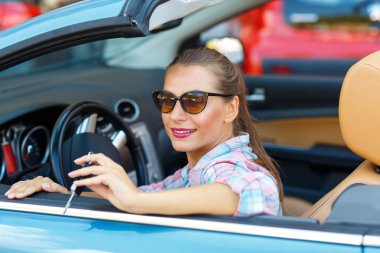 Woman in sunglasses sitting in a convertible car with the keys i