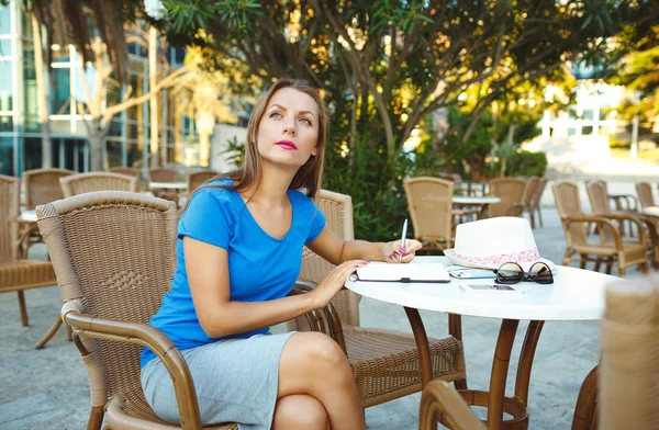 Jonge mooie vrouw maakt notities in een notitieblok in een café — Stockfoto