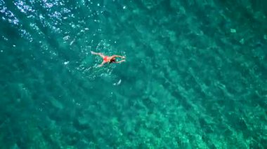 Pembe mayo giymiş bir kadının hava görüntüsü kristal berrak deniz sularında yüzüyor, rahatlatıcı bir şekilde. Yaz tatilleri.