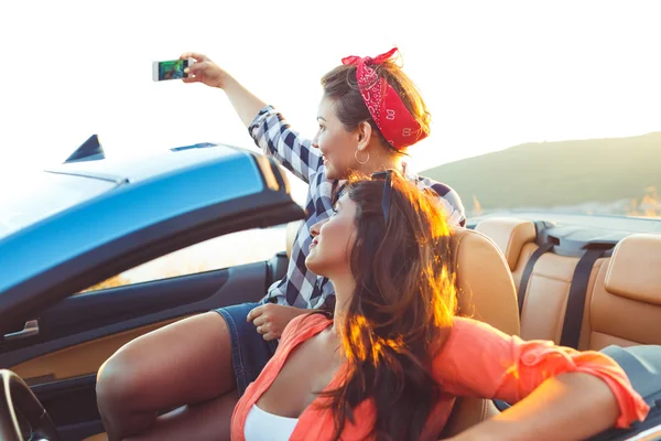 Duas meninas bonitas jovens estão fazendo selfie em um conversível — Fotografia de Stock