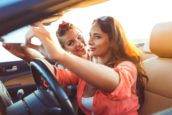 Duas meninas bonitas jovens estão fazendo selfie em um conversível — Fotografia de Stock