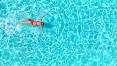 Pembe mayo giymiş bir kadının havuzda sırt üstü yüzüşü. Rahatlatıcı konsept, yaz yaşam tarzı. Yavaş çekim