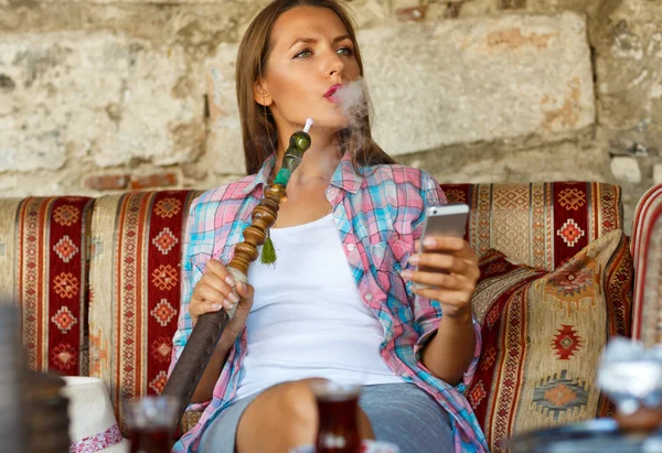 Woman smoking a hookah and uses smartphone in a cafe in Istanbul — Stockfoto