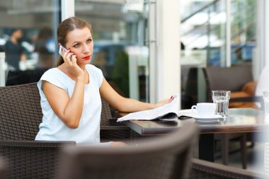 Cep telefonuyla konuşurken ve bir gazete okuyor genç kadın