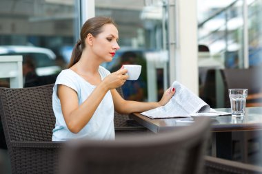 Bir gazete okuyor ve sabah içinde kahve içme genç kadın bir