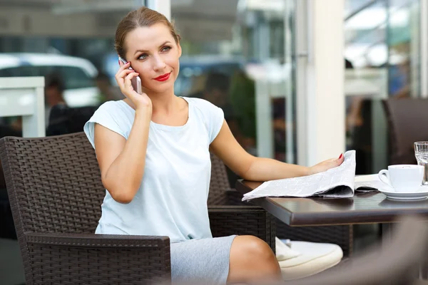 Cep telefonuyla konuşurken ve bir gazete okuyor genç kadın