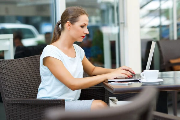 Joven mujer de negocios sentada en un café con una computadora portátil y café — Foto de Stock