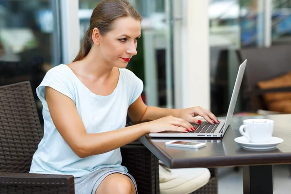 Giovane donna d'affari seduta in un caffè con un computer portatile e caffè — Foto Stock