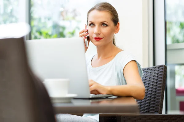 Jovem mulher sentada em um café com um laptop e falando sobre o c — Fotografia de Stock