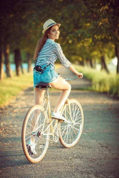 Adorável jovem mulher em um chapéu montando uma bicicleta em um parque — Fotografia de Stock