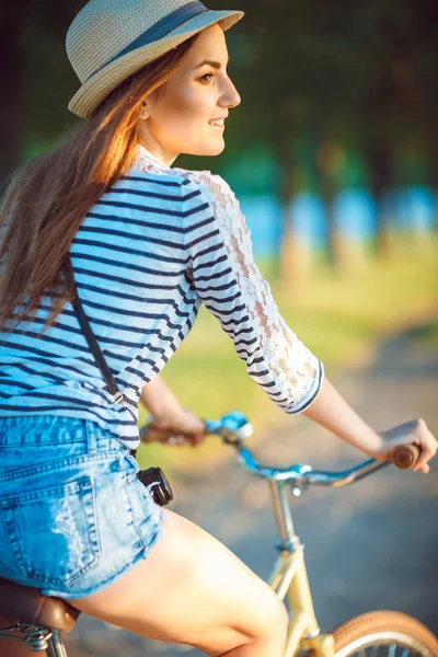 Adorável jovem mulher em um chapéu montando uma bicicleta em um parque — Fotografia de Stock