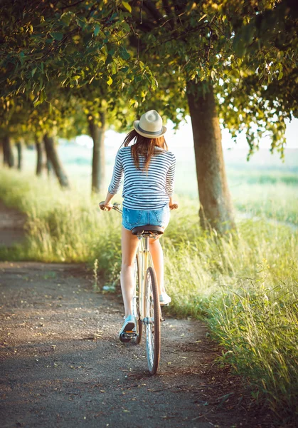 Mädchen mit Hut auf einem Fahrrad in einem Park - Blick von hinten — Stockfoto