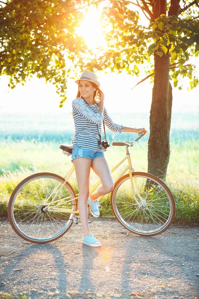 Preciosa joven en un sombrero montando una bicicleta en un parque — Foto de Stock