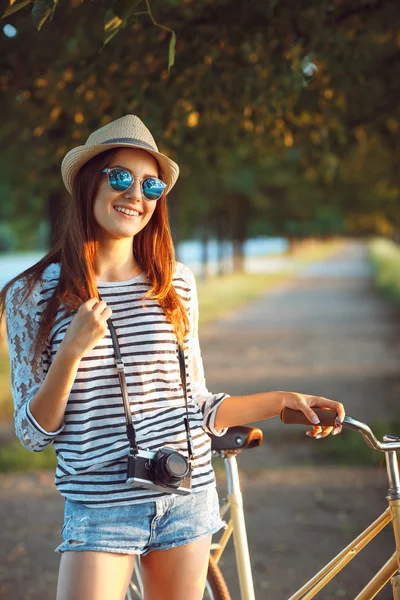 Wanita muda yang cantik dengan topi mengendarai sepeda di taman — Stok Foto