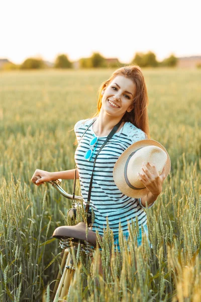 Wanita muda yang cantik berdiri di lapangan dengan sepedanya — Stok Foto