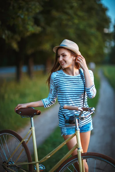 Прекрасна молода жінка в капелюсі з велосипедом в парку — стокове фото