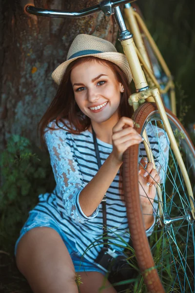 Härlig ung kvinna i en hatt med en cykel i en park — Stockfoto