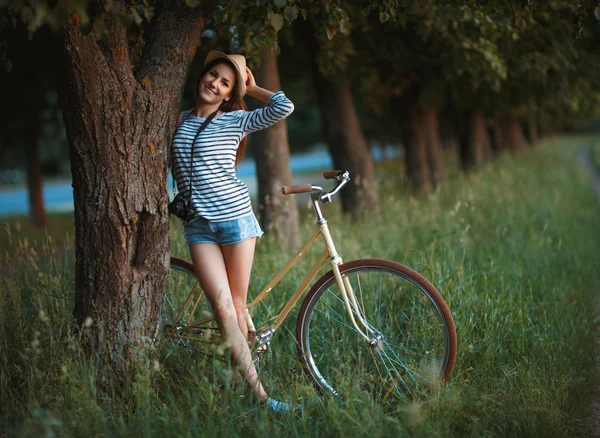 Lovely young woman in a hat with a bicycle in a park — Stock Photo, Image